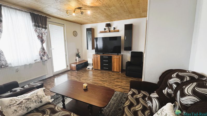 Obývací pokoj ve 4-pokojovém bytě s podlahou s dřevěným dekorem a televizorem na stěně.