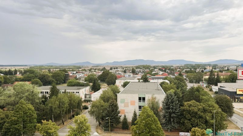 Pohled na Komenského ulici v Trebišově s budovami a zelení.