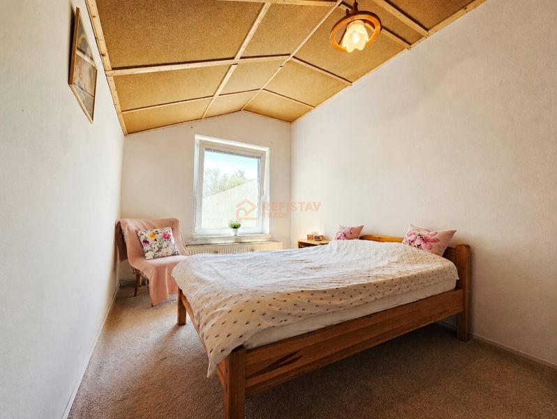Ložnice v rodinném domě s dřevěným stropem, kobercem a postelí s polštáři.