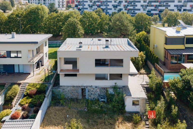 Rodinný dům na Komenského ulici v Banské Bystrici obklopený dalšími stavbami a zelení.