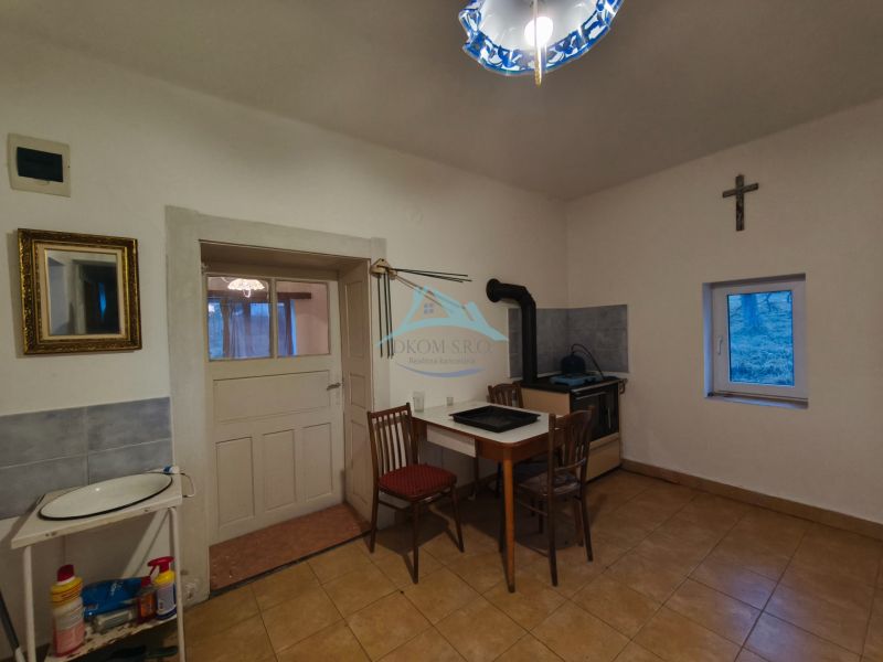 Kuchyně v rodinném domě s pecí, jednoduchým stolem a křeslem.