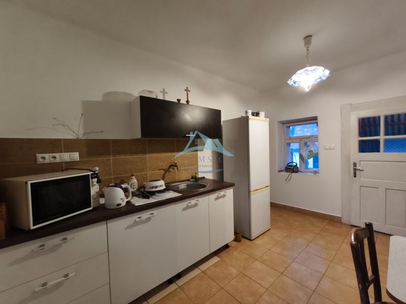Kuchyně v rodinném domě s hnědým obkladem, vybavená mikrovlnkou a ledničkou.