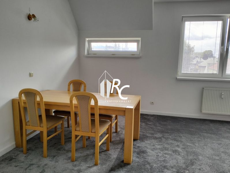 Stůl se čtyřmi židlemi v 2-pokojovém bytě, šedý koberec, dvě okna.