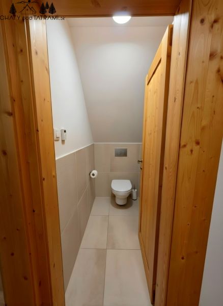 Interiér chaty s WC, světlé dlaždice a dřevěné obložení stěn dveří.