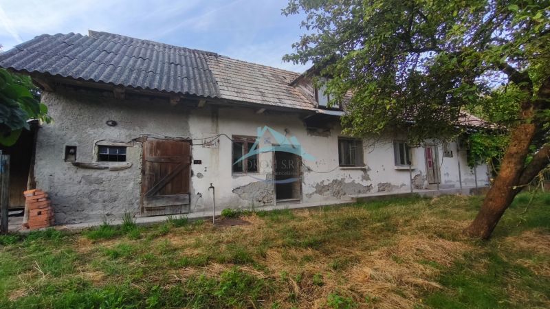 Rodinný dům v Čelovcích s opotřebovanou omítkou, dřevěnými dveřmi a zahradou.