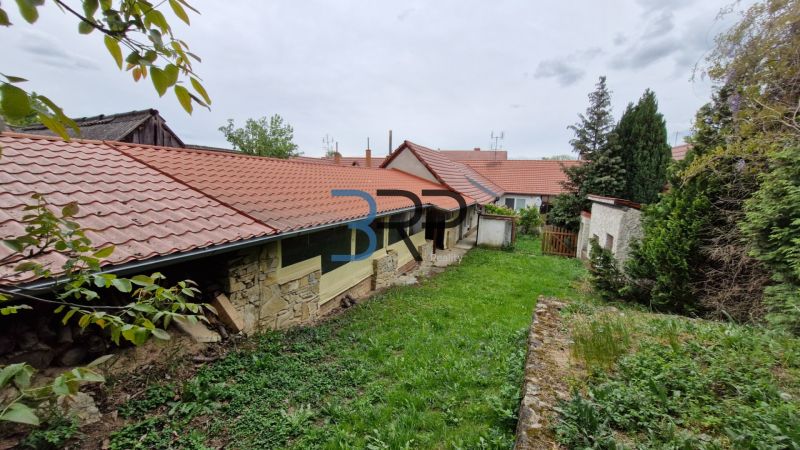 Zahrada u rodinného domu v Mokrém Háji s kamennou zdí a červenou střešní krytinou.