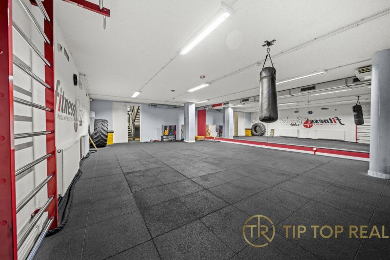 Fitness prostor s boxovacím pytlem, velkými zrcadly a černou podlahou.