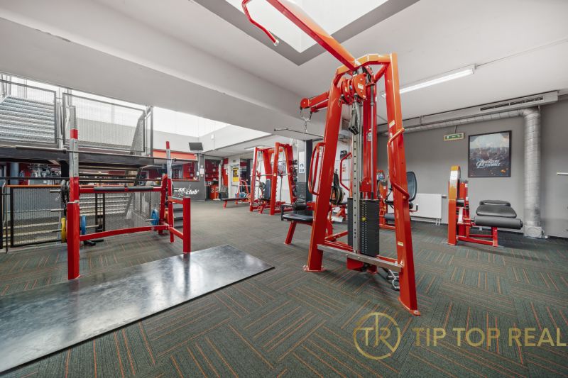 Fitness centrum s činkami a posilovacími stroji, obchodní prostory.