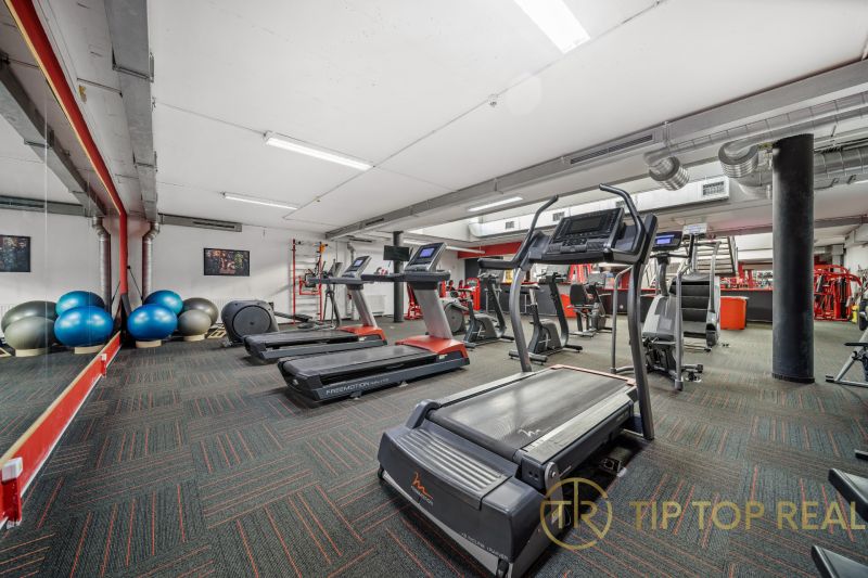 Fitness centrum s běžeckými pásy a cvičebními pomůckami v obchodních prostorech.