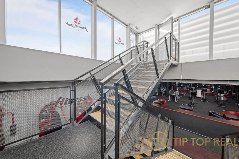 Ocelové schodiště v dvoupodlažních obchodních prostorách s fitness zařízeními.