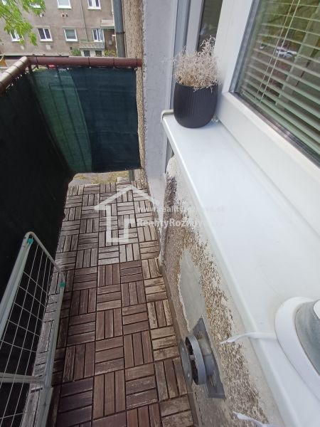 Balkon v 2-pokojovém bytě s podlahou s dřevěným dekorem a květináčem.