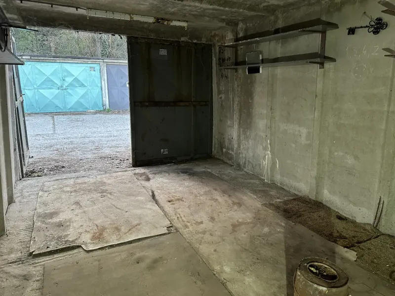 Interiér garáže s betonovou podlahou a kovovými regály.