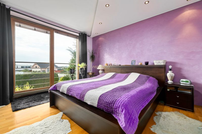 Stylová ložnice s fialovou stěnou a výhledem, podlaha s dřevěným dekorem.