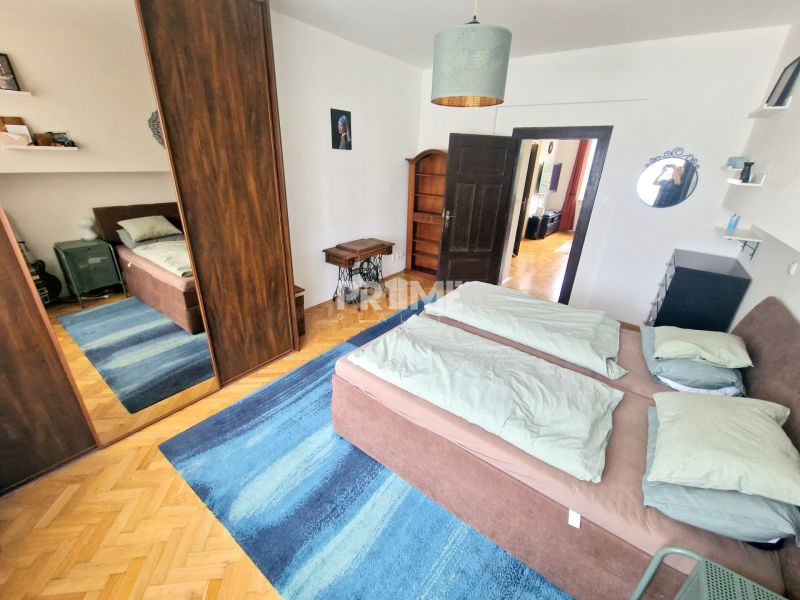 Ložnice v třípokojovém bytě s postelí, zrcadlovou skříní a modrým kobercem.