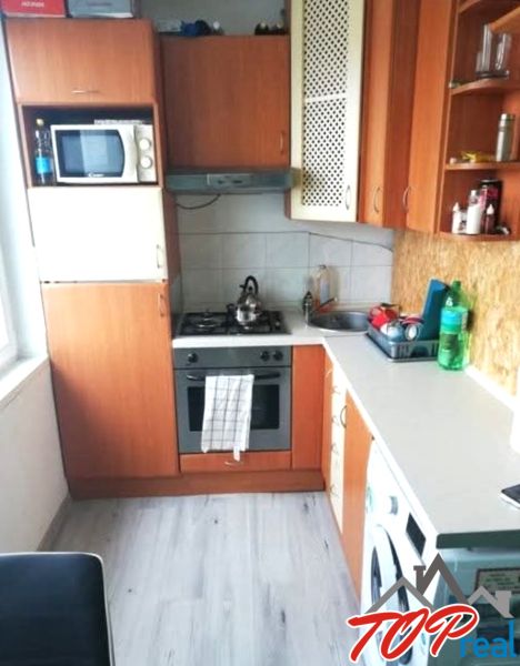 Kuchyně v 1-pokojovém bytě s podlahou s dřevěným dekorem, základními spotřebiči a skříňkami.