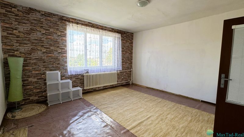 Pokoj s velkým oknem, kobercem a cihlovým vzorem stěn v rodinném domě.