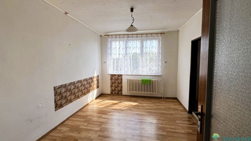 Pokoj v rodinném domě s podlahou s dřevěným dekorem, závěsem a radiátorem pod oknem.