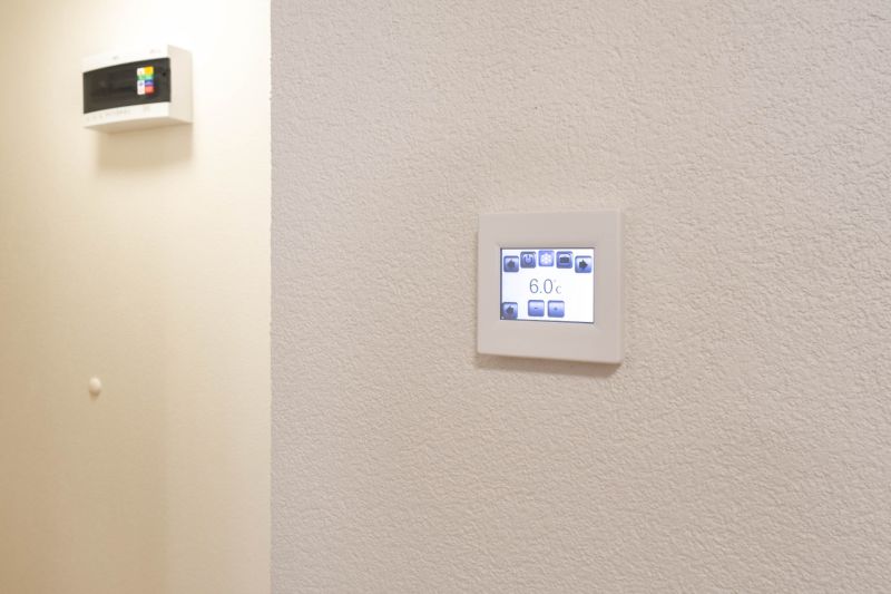 Nastavitelný termostat na stěně v garsonce, jednoduchý design, bílé pozadí.