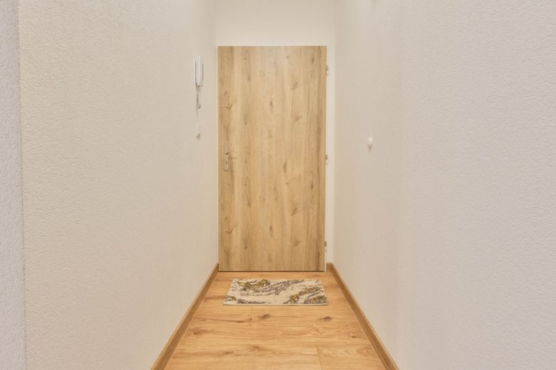 Úzká chodba s bílými stěnami a dveřmi s dřevěným dekorem v garsonce.