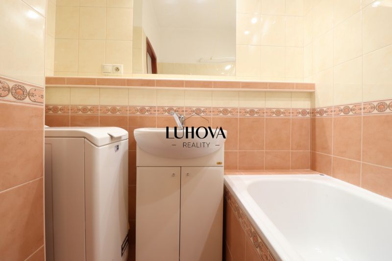 Koupelna v 2-pokojovém bytě s vanou a pračkou, obložená barevnými dlaždicemi.