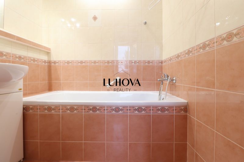 Koupelna v 2-pokojovém bytě s vanou a umyvadlem obložená béžovými a růžovými kachličkami.