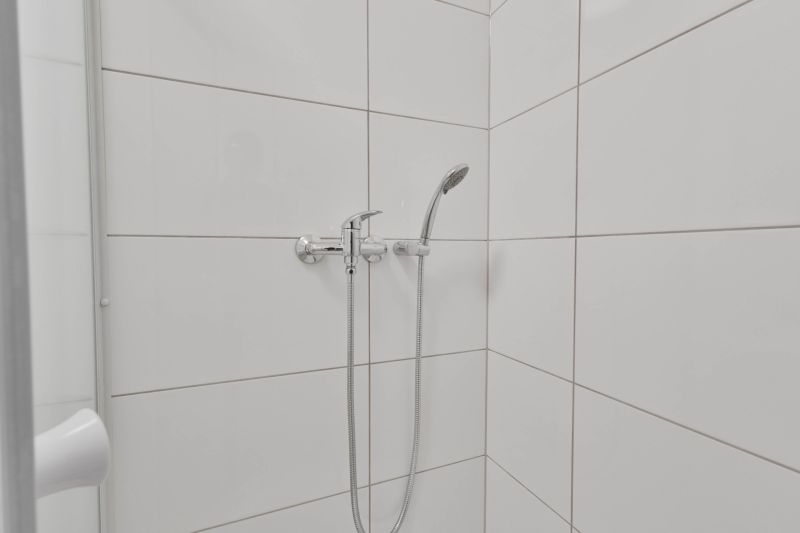 Sprchový kout s bílými obkladačkami a sprchovou hlavicí v garsonce.
