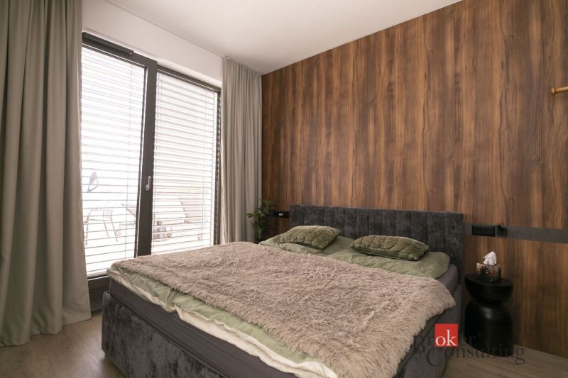 Dvojlůžková postel s měkkou přikrývkou v 2-pokojovém bytě s podlahou s dřevěným dekorem.