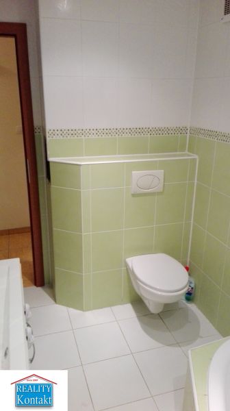 Koupelna s bílými a zelenými obklady ve 3-pokojovém bytě, WC a umyvadlo.