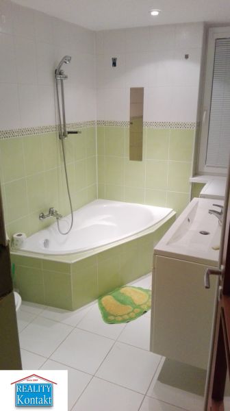 Koupelna s rohovou vanou a zelenými obklady v 3-pokojovém bytě.