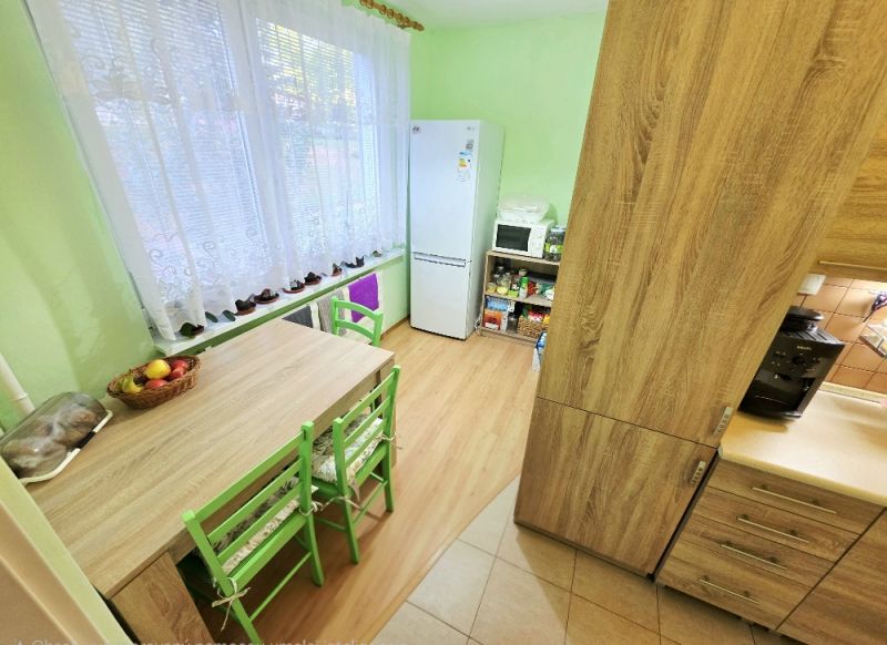 Kuchyně ve 4-pokojovém bytě se stolem, zelenými židlemi a podlahou s dřevěným dekorem.
