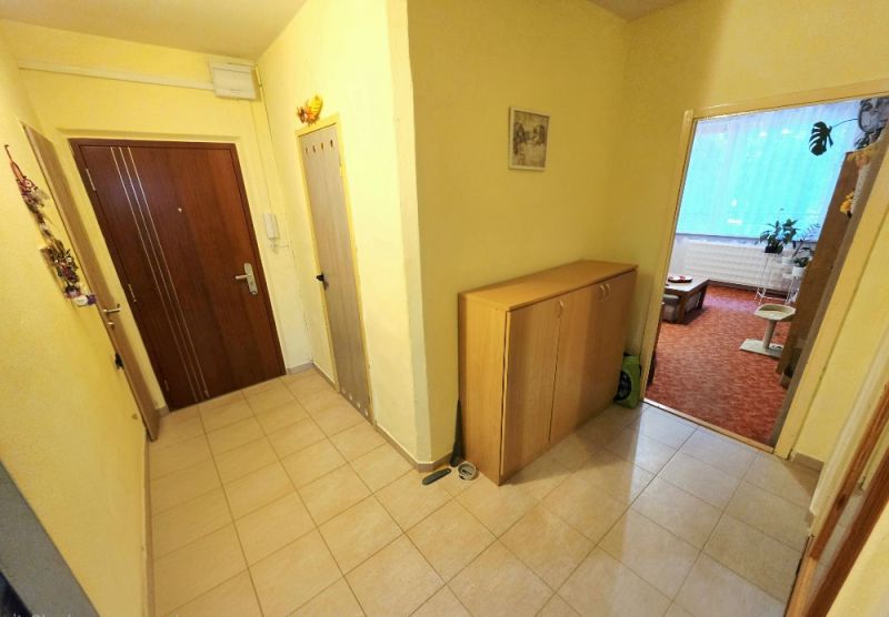 Předsíň ve 4-pokojovém bytě se vstupními dveřmi a nábytkem na odkládání.