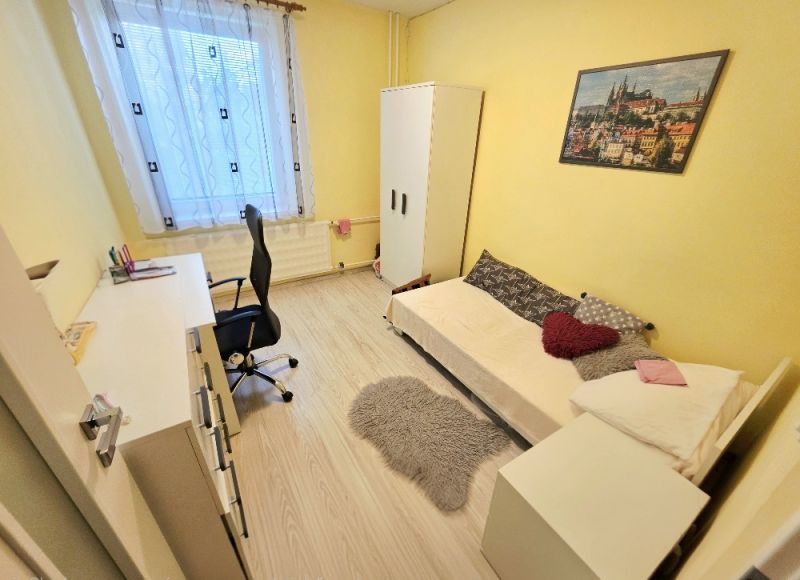 Žlutý pokoj s jedním lůžkem, pracovním stolem a podlahou s dřevěným dekorem ve 4pokojovém bytě.