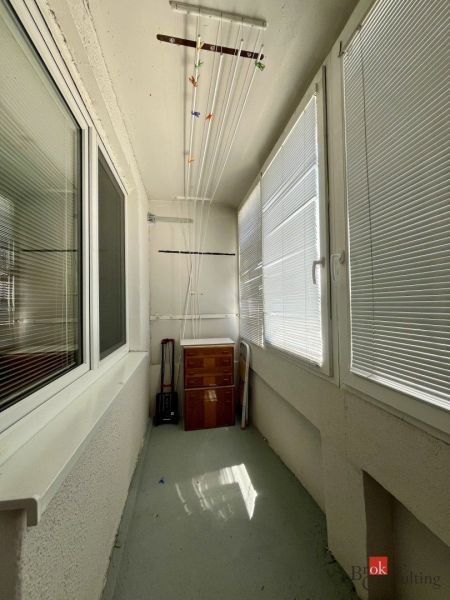 Zasklený balkon s dřevěnou skříňkou a sušákem, součást garsonky.