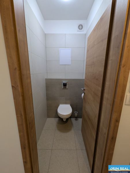 Toaleta v 2-pokojovém bytě s keramickými obklady a podlahou s dřevěným dekorem.