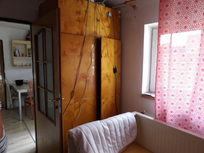 Pokoj v 2pokojovém bytě s otevřenými dveřmi, skříňkou a závěsem s červeným vzorem.