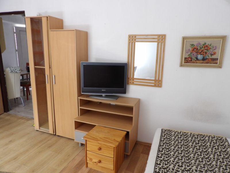 Televizor na nízké skříňce, skříň a zrcadlo v 2-pokojovém bytě s podlahou s dřevěným dekorem.
