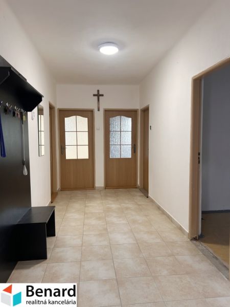 Chodba v rodinném domě s dlažbou, dřevěnými dveřmi a věšákem.