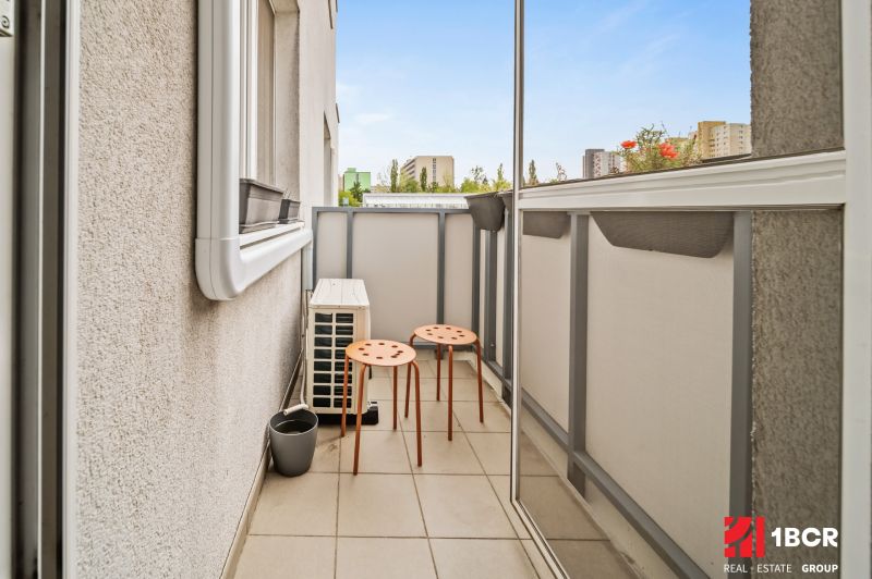 Balkon se dvěma oranžovými židlemi v 2-pokojovém bytě s výhledem na město.