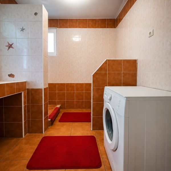 Koupelna v rodinném domě se sprchovým koutem a pračkou, dlažba v odstínech hnědé.