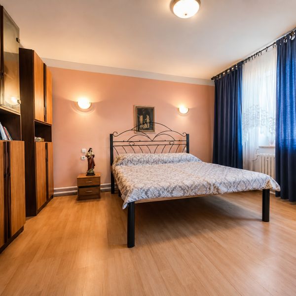 Ložnice s kovovou postelí, podlaha s dřevěným dekorem, nábytek a závěsy v rodinném domě.