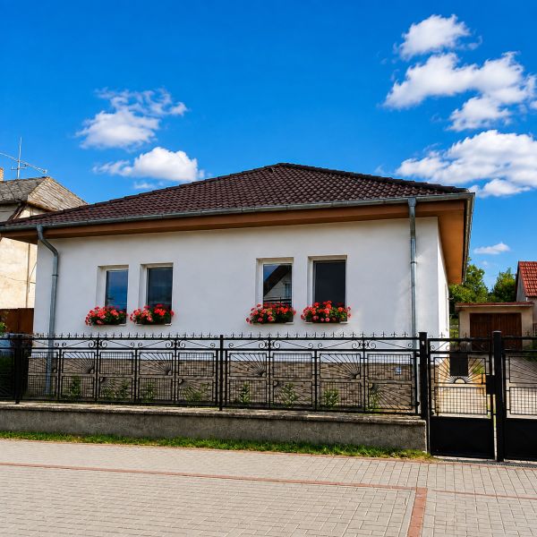 Rodinný dům v Šalgočce s bílou fasádou, okenními květinami a valbovou střechou.