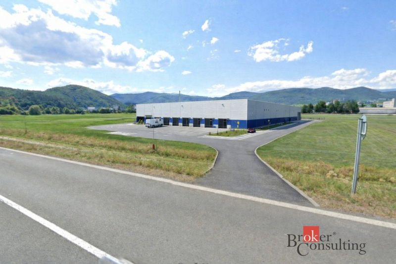 Komerční pozemky v Hliníku nad Hronom s průmyslovou halou, obklopené kopcovitou krajinou.