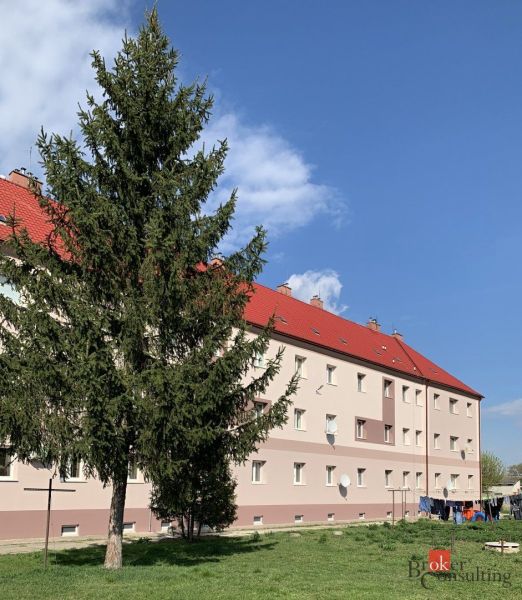 Budova s červenými střechami a před ní strom, na Železniční ulici v Šahách.