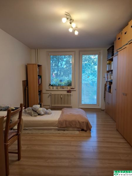 Pokoj v 3-pokojovém bytě s postelí, policemi a podlahou s dřevěným dekorem.