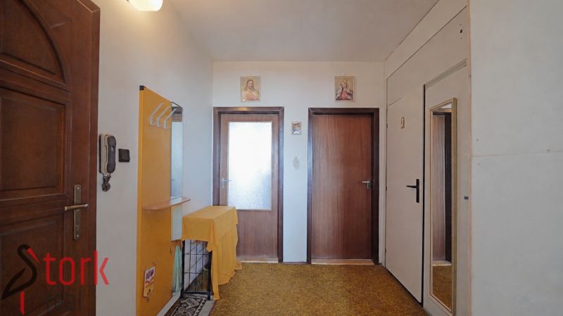 Vstupní předsíň v 2-pokojovém bytě s dřevěnými dveřmi a zrcadlem na stěně.