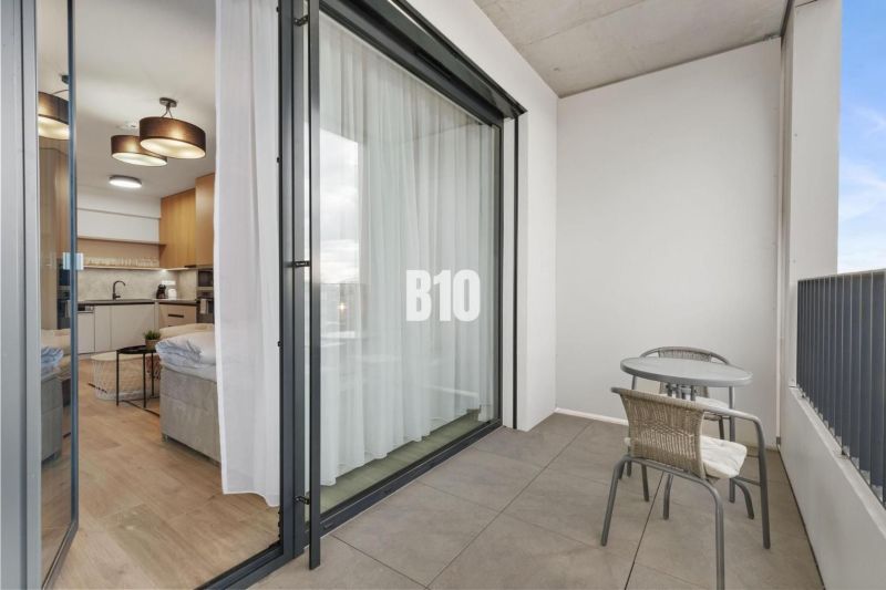 Balkon s posezením a výhledem do 1-pokojového bytu přes posuvné dveře.
