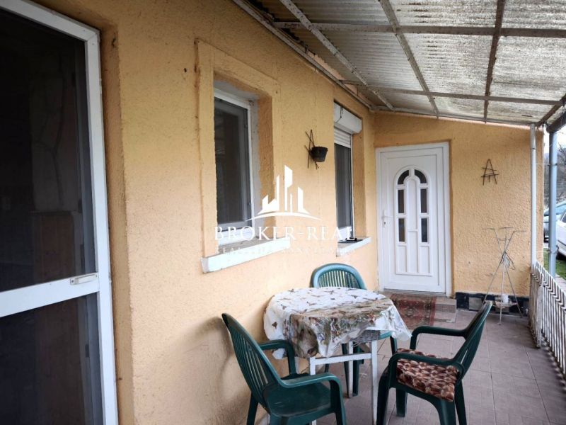 Terasa rodinného domu v Bódvaszilasu se stolem a plastovými židlemi na dlážděné podlaze.