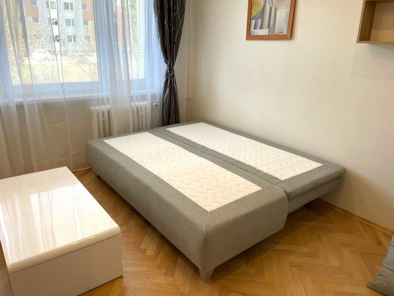 Garsonka s postelí, podlahou s dřevěným dekorem a bílým stolkem.