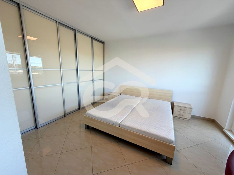 Světlá ložnice s posuvnou skříní, postelí a dlaždicovou podlahou v 1-pokojovém bytě.