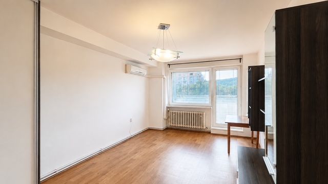 Obývací pokoj s podlahou s dřevěným dekorem, klimatizací a velkým oknem ve 3pokojovém bytě.